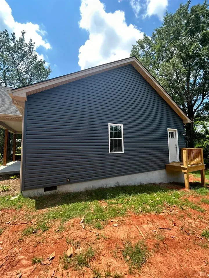 A side view of a house with dark blue siding, a single window, a white door with a small wooden deck, and a concrete base.