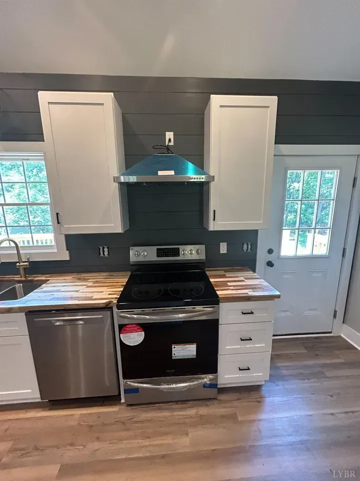 A modern kitchen with white cabinets, wood countertops, stainless steel appliances, and a dark shiplap backsplash.