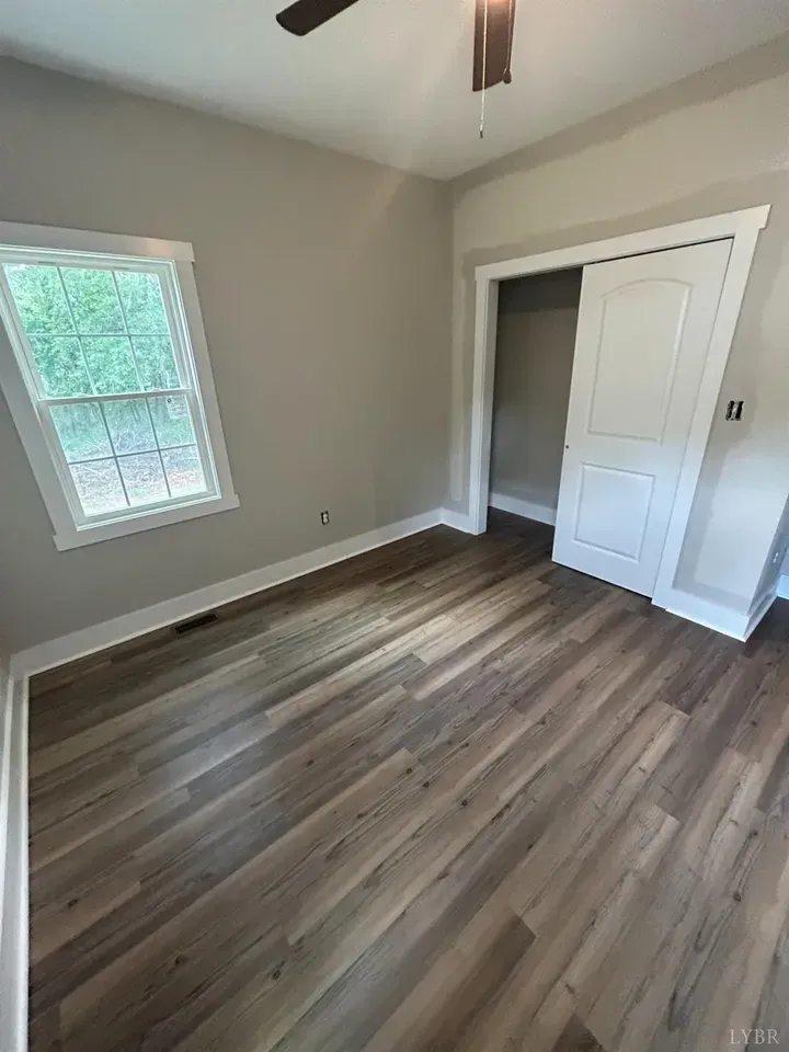 Empty room with light gray walls, wood-look plank flooring, a window on the left, and a white closet door on the right.