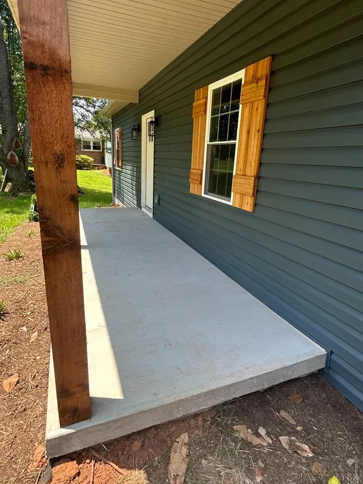 A grey house with a concrete porch, a wooden support post, and a window with wooden shutters.