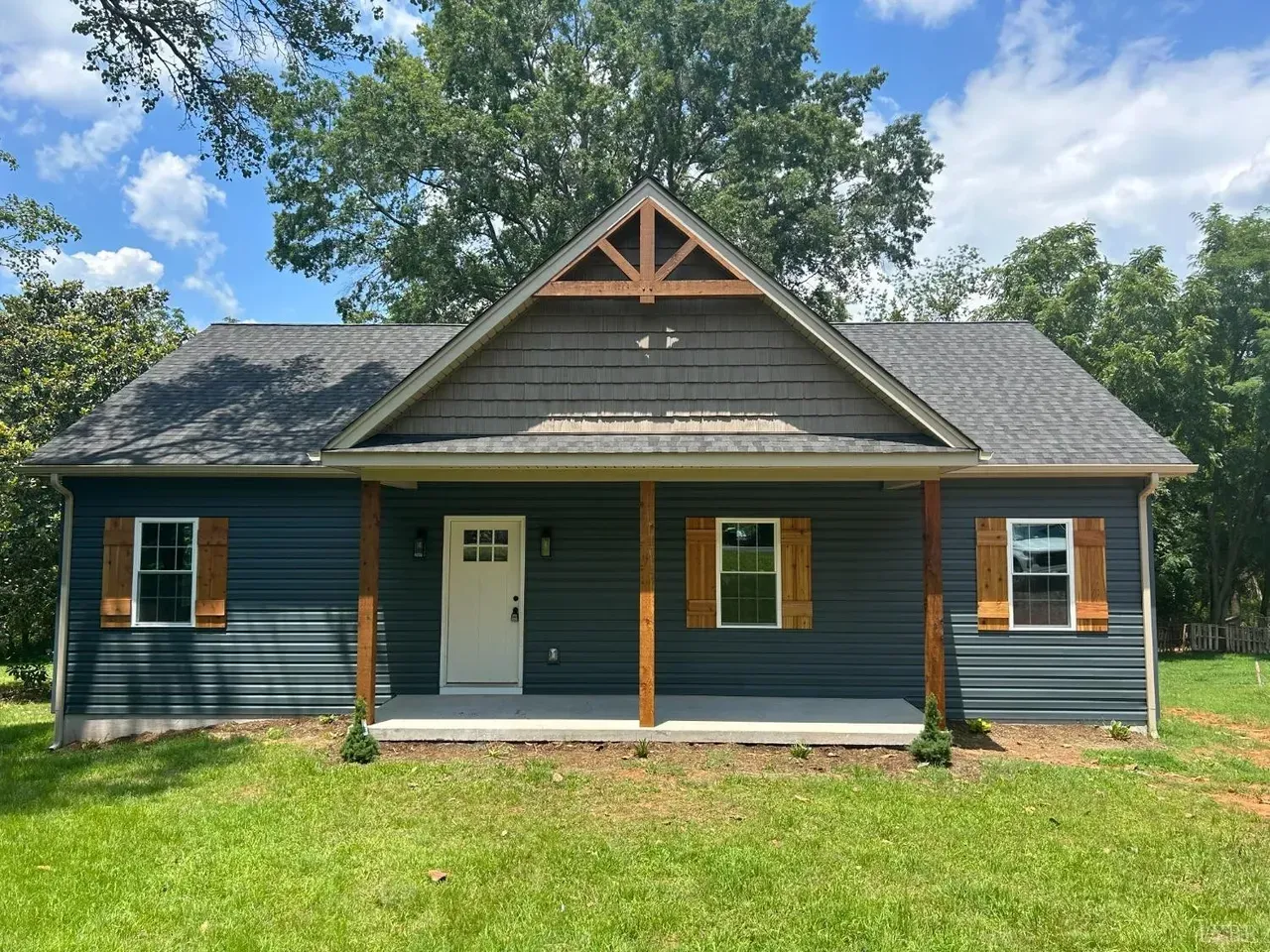 A single-story blue house with a covered front porch, white door, wooden shutters, and a triangular gable roof design.