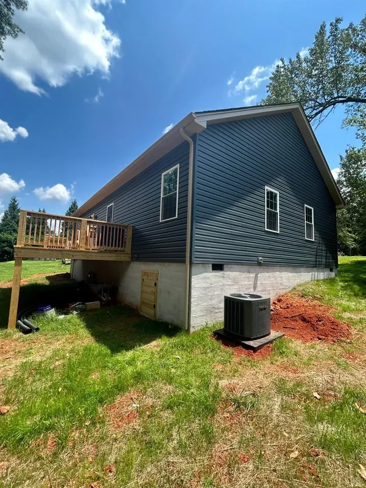 A dark-blue sided house with a wooden deck, a concrete foundation, and an outdoor HVAC unit on a grassy lawn.