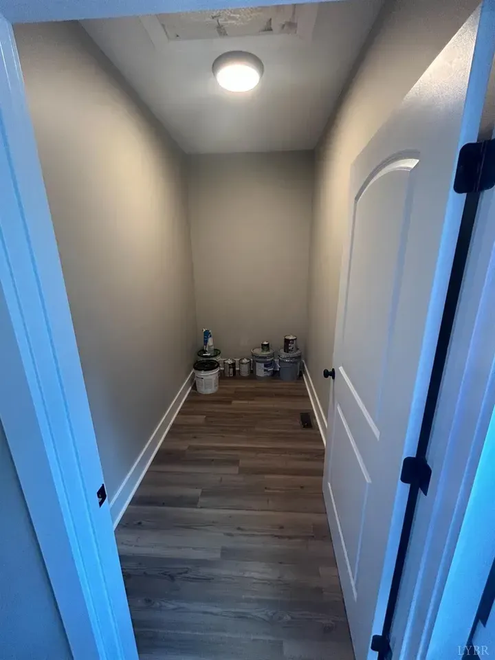 A view into a small, empty walk-in closet with neutral walls, wood-look flooring, and a few paint cans on the floor.
