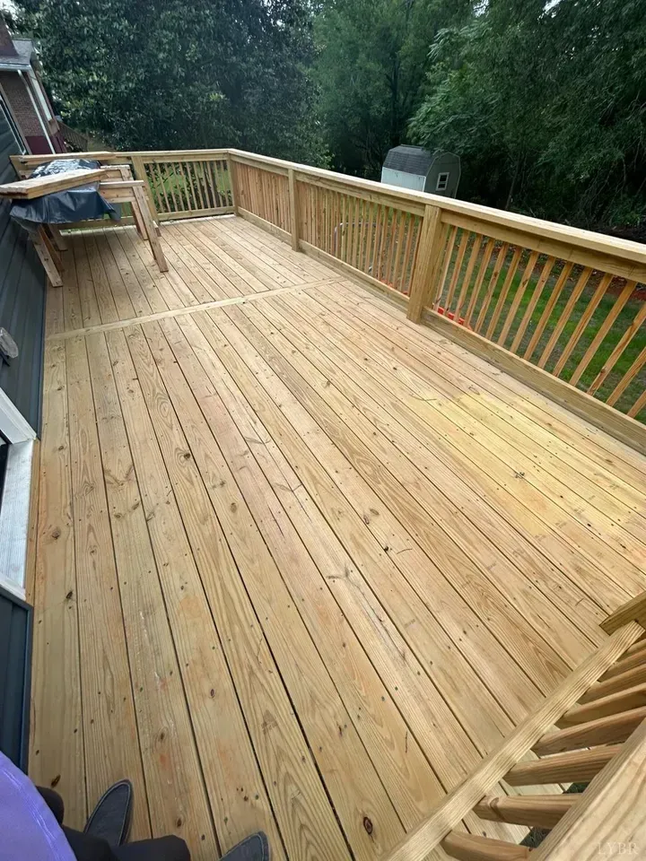 A newly stained, light-brown wooden deck with railings, viewed from above, with a table partially visible on the left.
