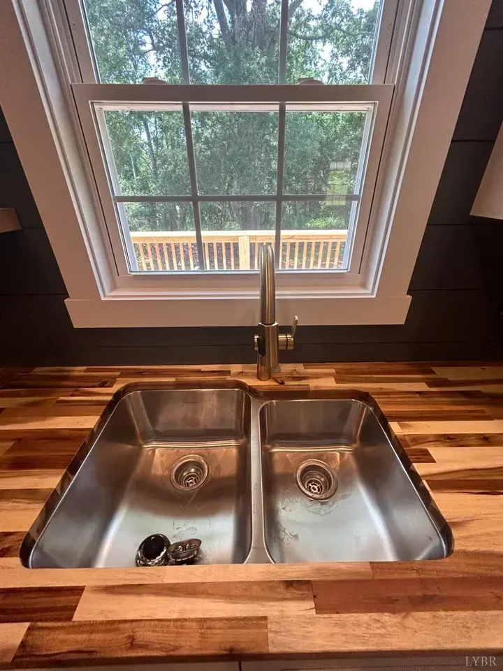 A stainless steel double-basin kitchen sink with a metal faucet, set into a wood countertop in front of a window.