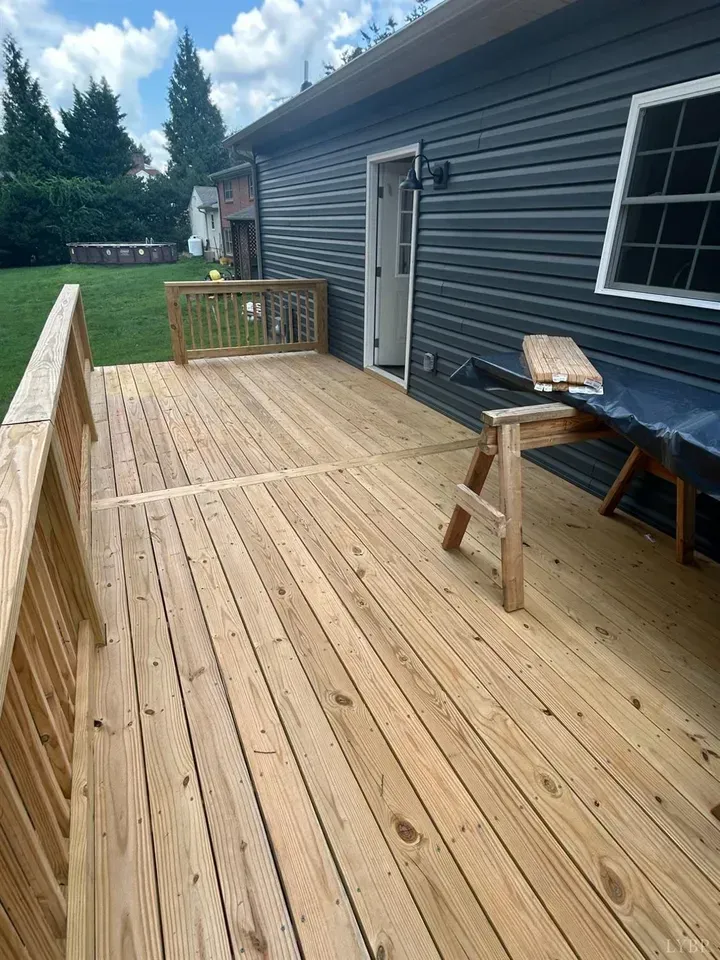A newly built wooden deck with railings attached to a house with dark gray siding, featuring a wooden sawhorse.