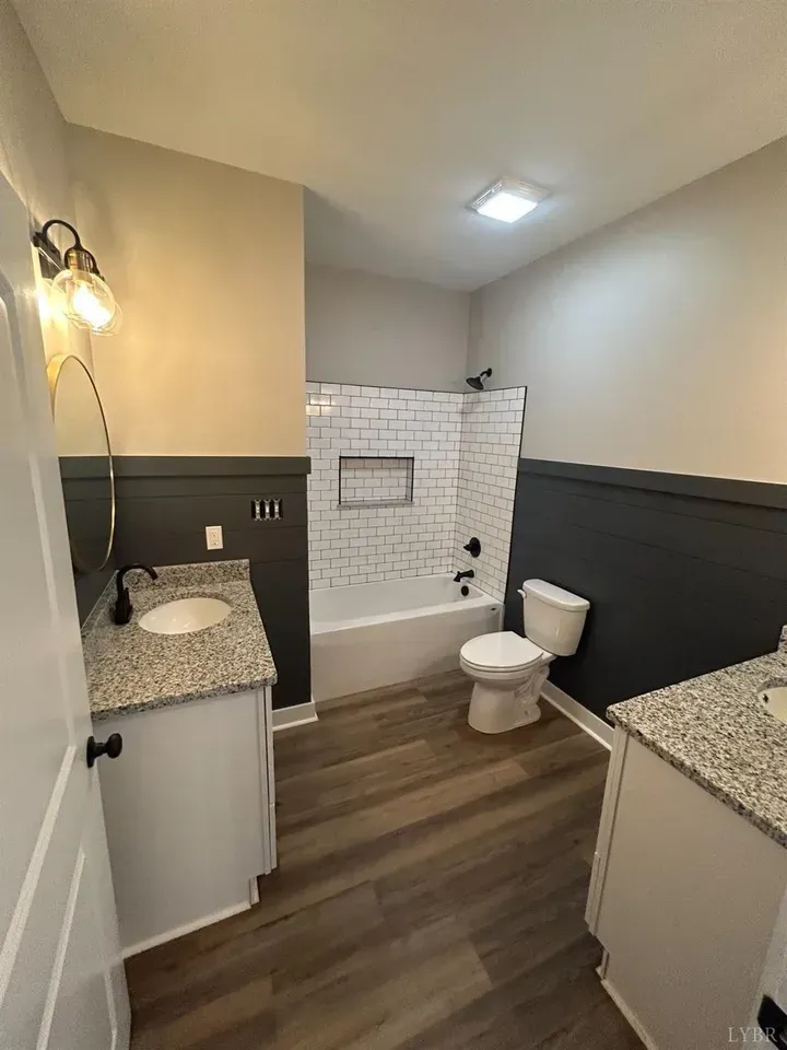 A bathroom with grey walls, granite vanity tops, wood-look floors, and a white subway tile shower surround.
