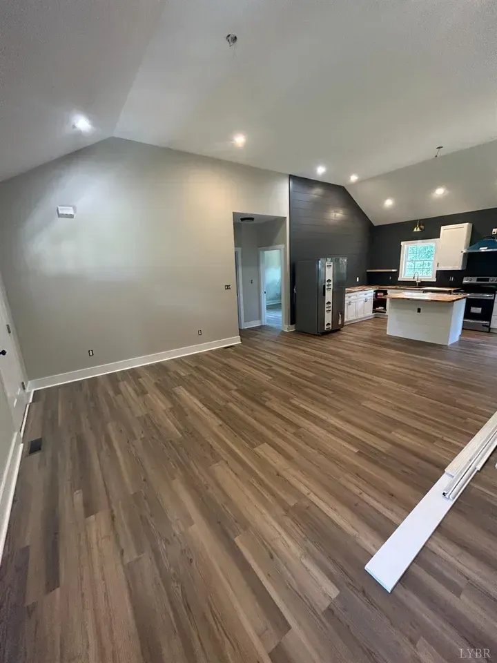 An open-concept living area with light gray walls, dark wood-look flooring, and a kitchen with a white island.