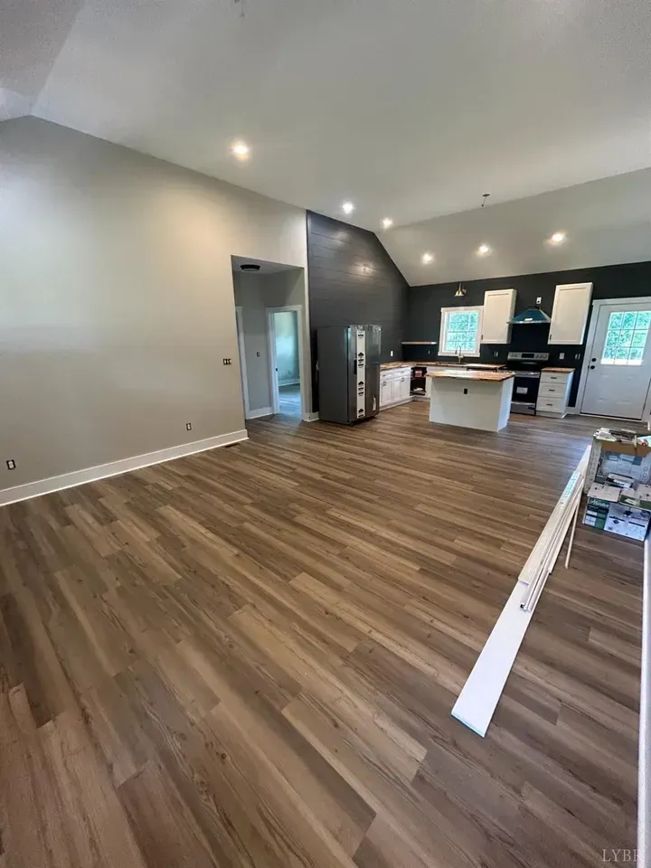 An open-plan living and kitchen area featuring light-toned walls, dark accent cabinets, wood-look flooring, and a kitchen.