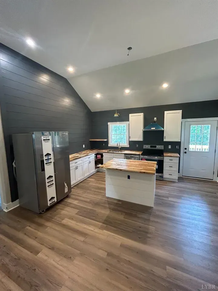 Modern kitchen featuring white cabinets, a wood-topped island, stainless steel refrigerator, and dark charcoal shiplap walls.