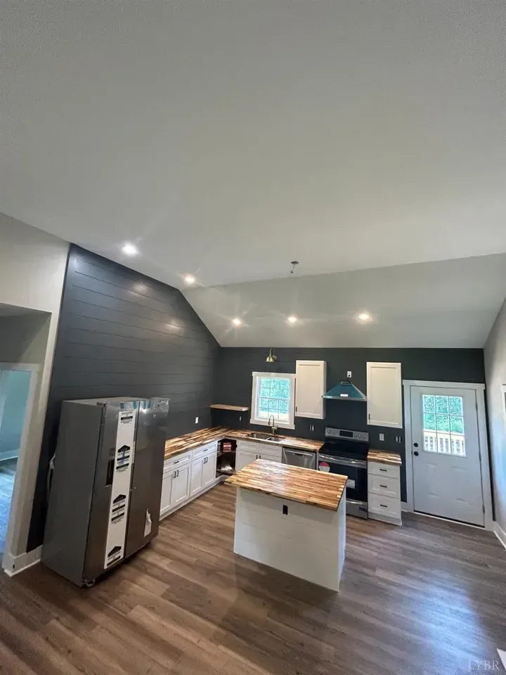 A kitchen featuring white cabinets, a wood-topped island, a refrigerator, and dark gray shiplap walls in a vaulted space.
