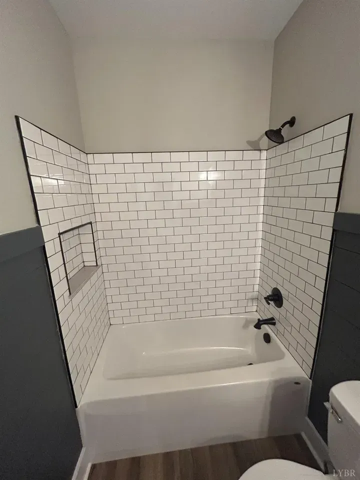 A white bathtub with a white subway tile surround, featuring a built-in recessed shelf and black shower fixtures.