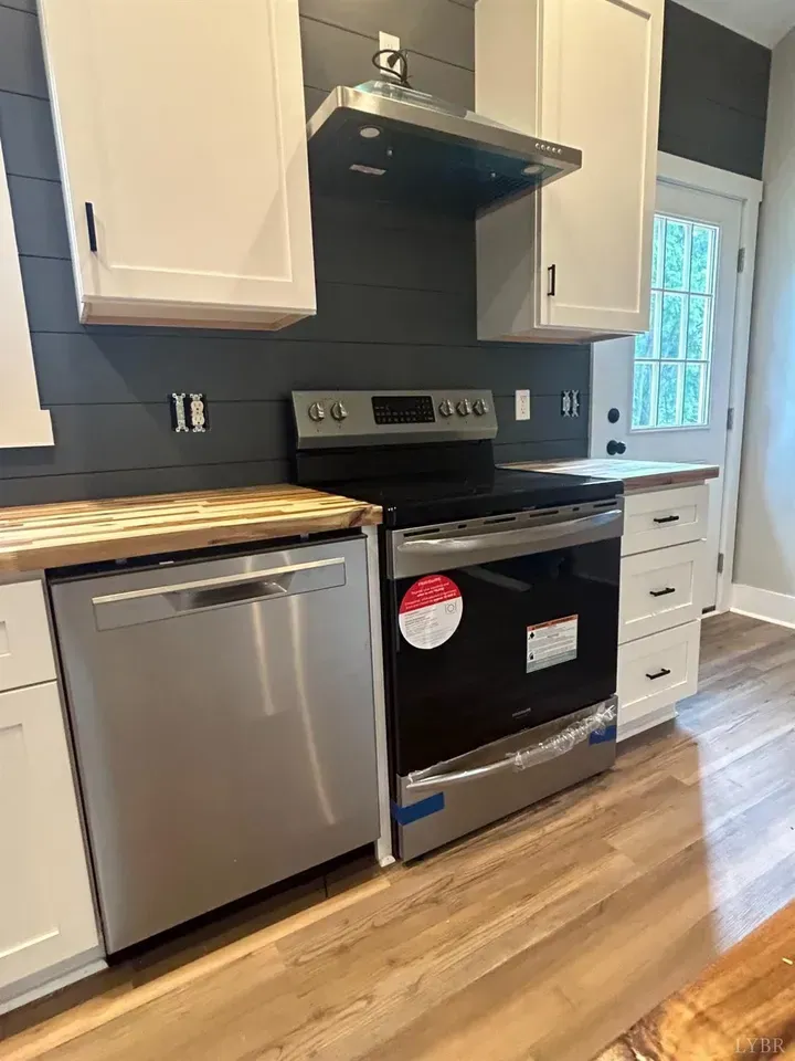 A modern kitchen with white cabinets, stainless steel appliances, a range hood, and dark grey shiplap walls.
