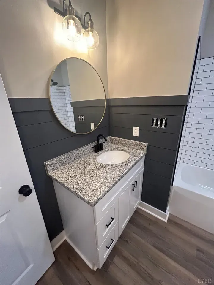 A modern bathroom with a white vanity, speckled countertop, round mirror, and dark grey shiplap walls.