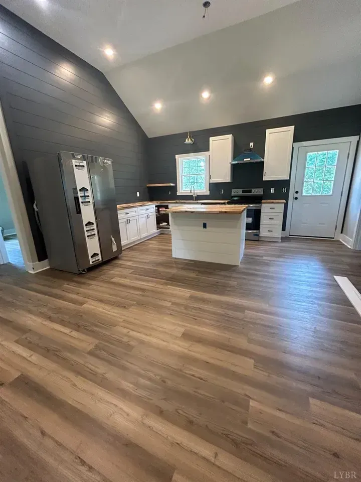 A modern, open-concept kitchen featuring dark shiplap walls, white cabinetry, a wood-topped island, and light wood flooring.