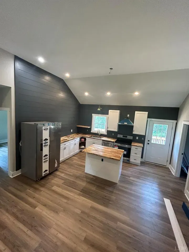 An open kitchen featuring white cabinets, a wood-topped island, a tall grey refrigerator, and a dark shiplap accent wall.