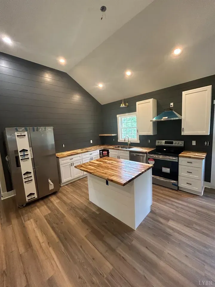 A modern kitchen featuring white cabinets, wood-topped island, dark gray shiplap walls, and stainless steel appliances.