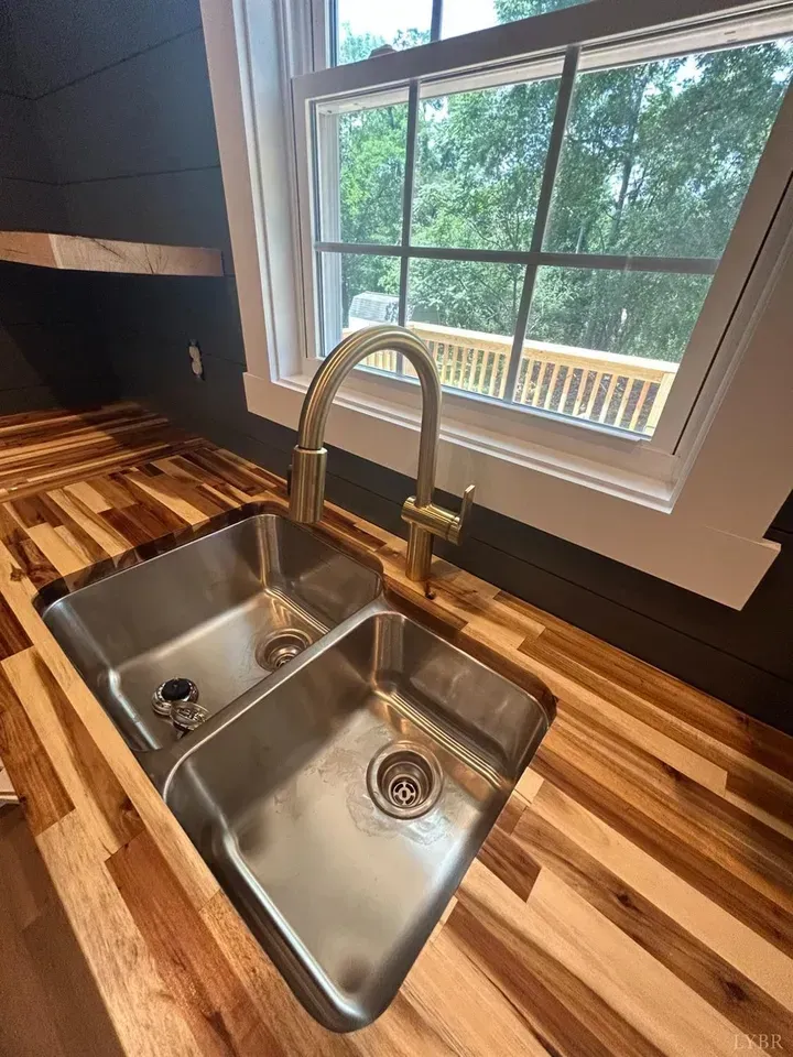 A stainless steel double-basin kitchen sink with a gold faucet, set into a natural wood butcher block countertop.
