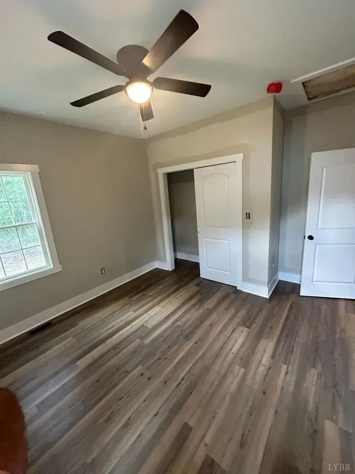 A room with light wood-look flooring, beige walls, a ceiling fan, a window, and two white doors.