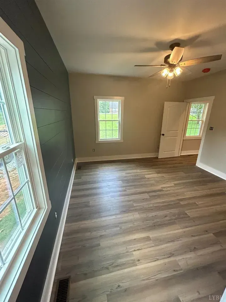 An empty room with dark shiplap on one wall, grey wood-look flooring, light grey walls, and a ceiling fan.