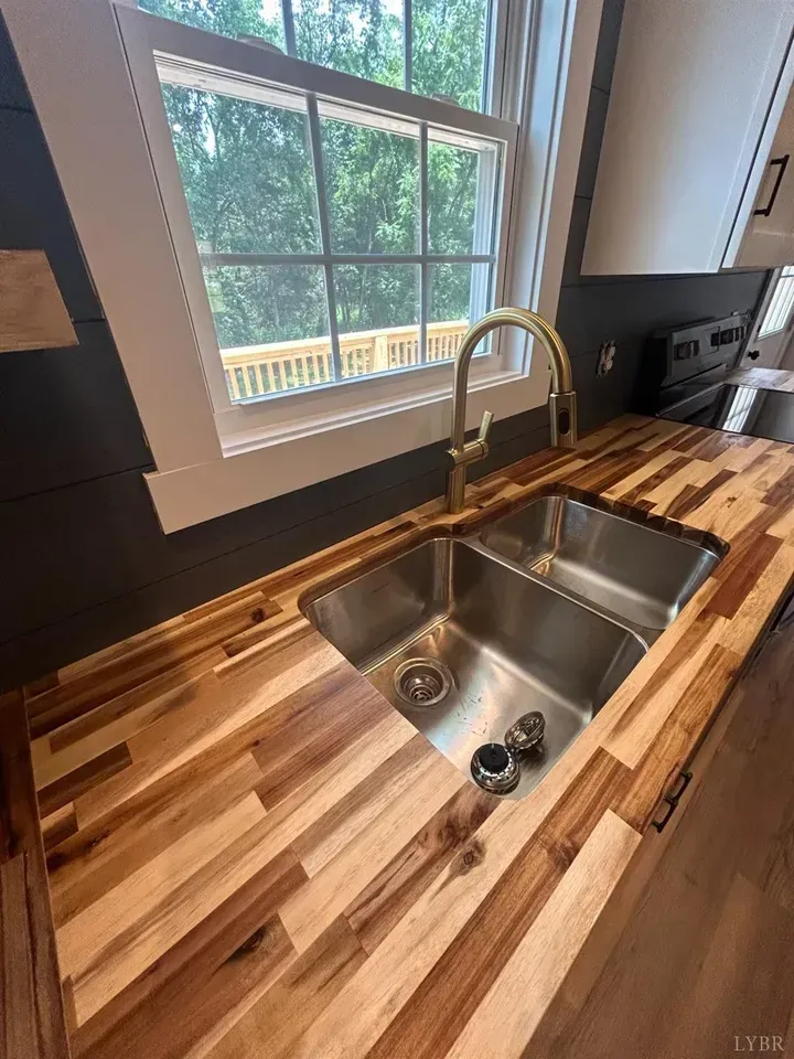 A modern kitchen with dark shiplap walls, white cabinetry, a central island, and wood-look flooring under a vaulted ceiling.
