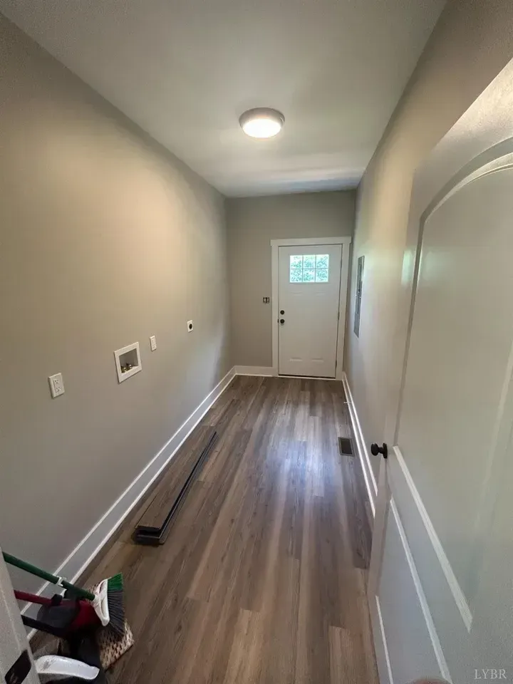 A hallway with light gray walls, wood-look flooring, a flush-mount ceiling light, and a white door at the end.