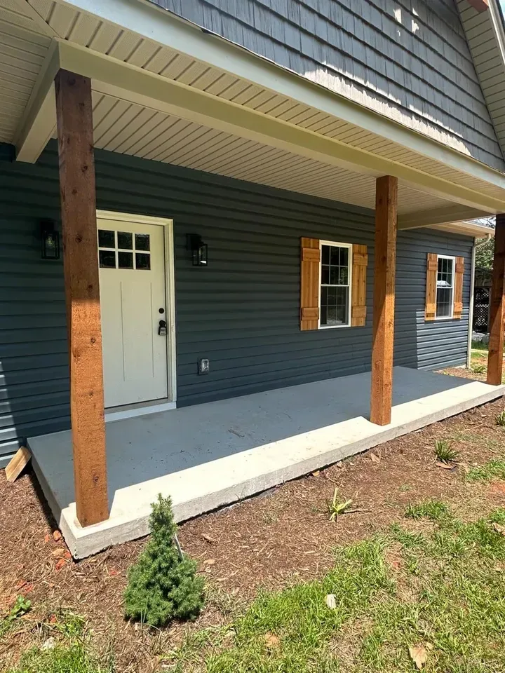 A porch with a white door, two wooden posts, and wooden shutters on dark blue horizontal siding.