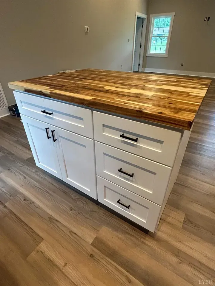 A kitchen island with white cabinets, black handles, and a butcher block wood countertop on light wood flooring.