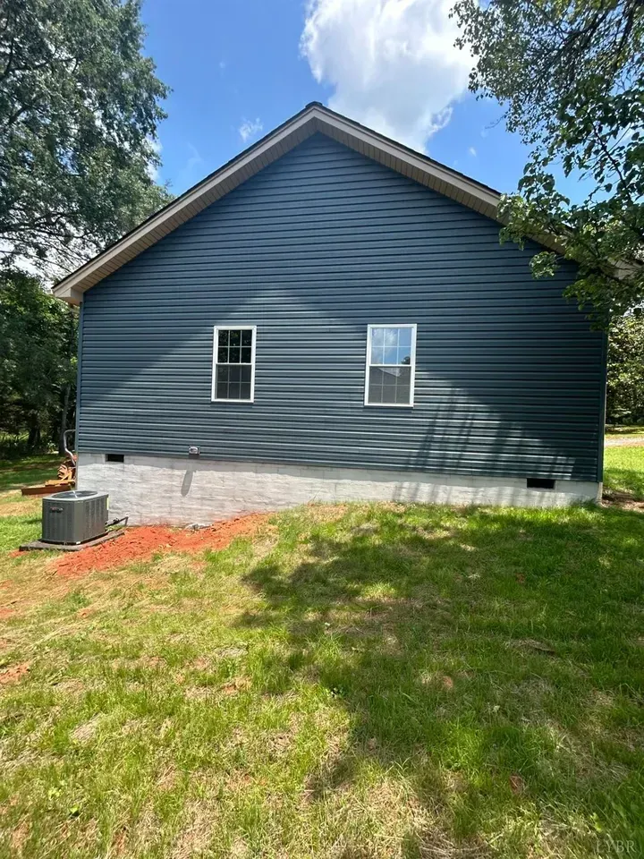 Blue-sided house with a light stone foundation, two windows, and an outdoor HVAC unit in a sunny, grassy yard.