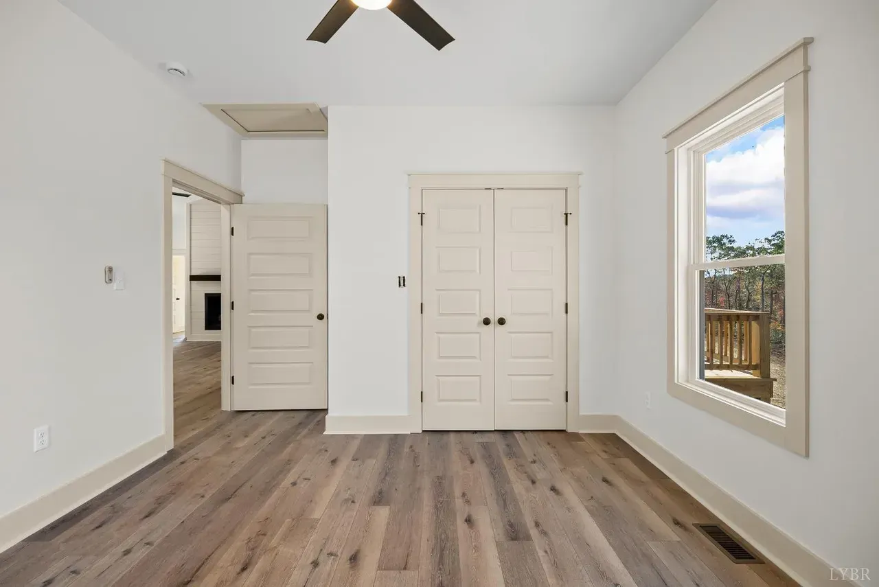 A bright, modern room featuring white walls, wood floors, double doors, a single doorway, and a window with outdoor views.