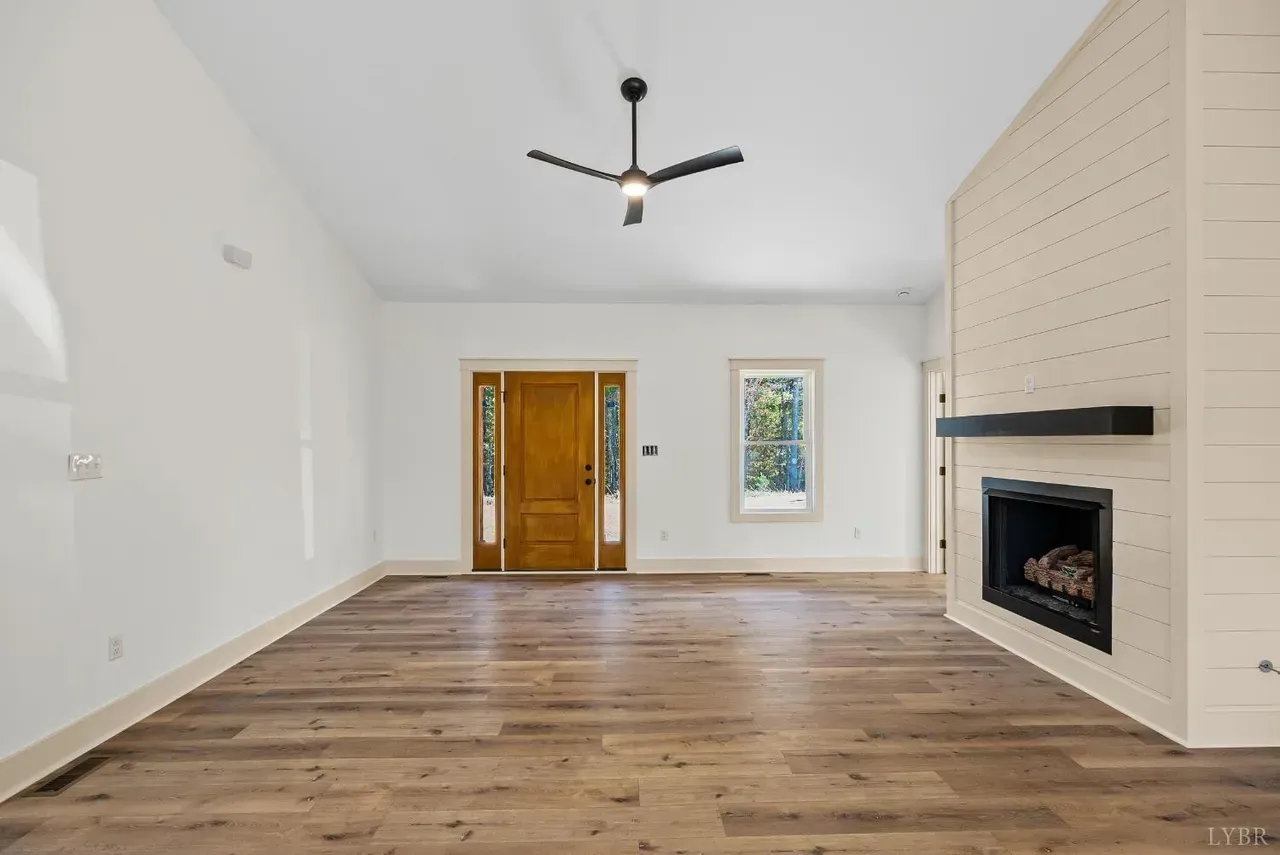 A vacant living room featuring white walls, light wood flooring, a shiplap fireplace, and a wooden front door.