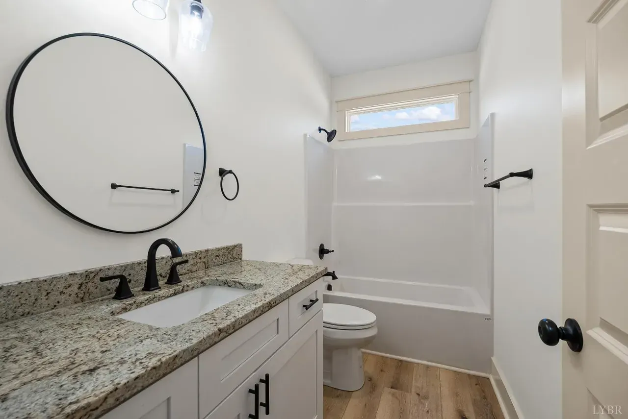 Modern bathroom with a round mirror over a granite vanity, white cabinets, and a bathtub shower combination.