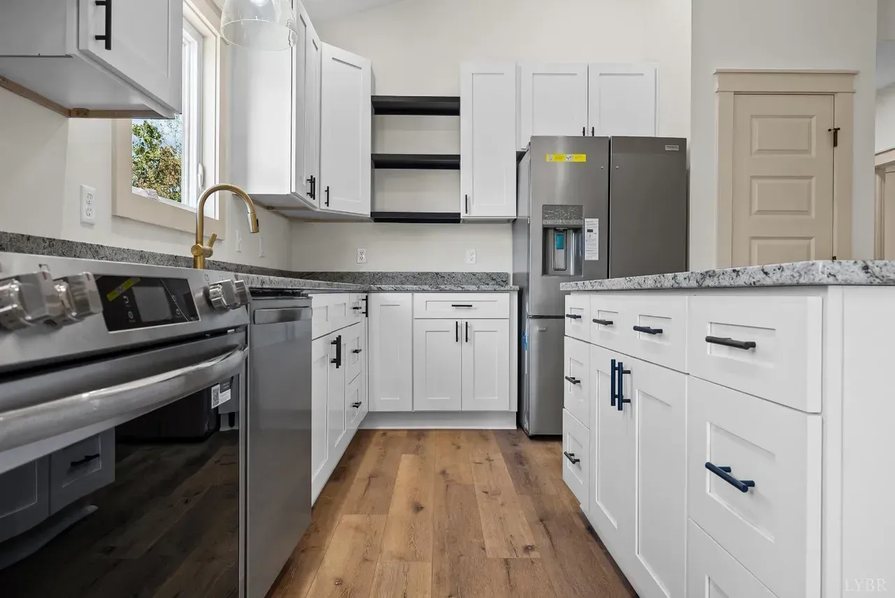 A modern kitchen with white cabinets, speckled grey countertops, stainless steel appliances, and wood flooring.