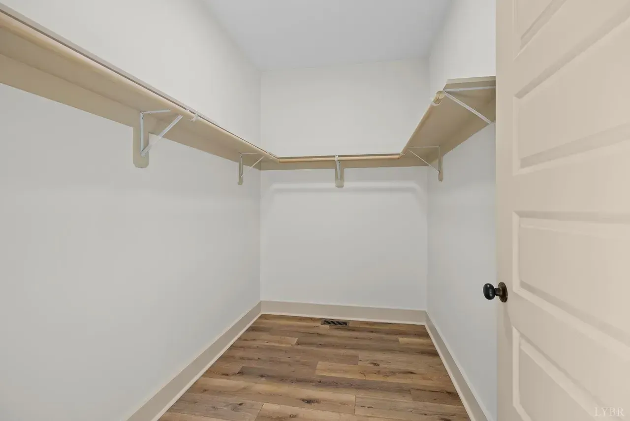 An empty, walk-in closet with white walls, wood-look flooring, and white wire shelving on three sides.