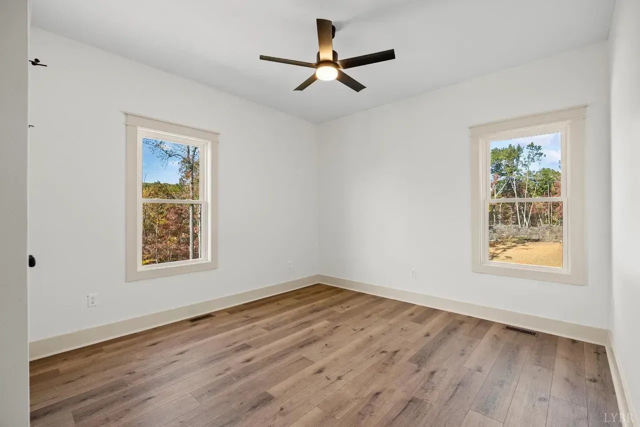 A bright, empty room with white walls, wood-look flooring, two windows, and a ceiling fan.