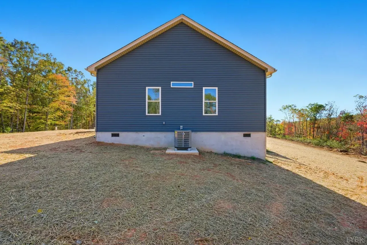 A side view of a blue, single-story house with two small windows and an air conditioning unit on a gravel lot.