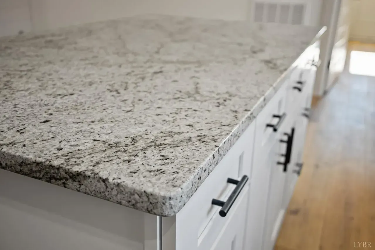 A close-up view of white granite countertops with dark gray flecks on white cabinets with black hardware.