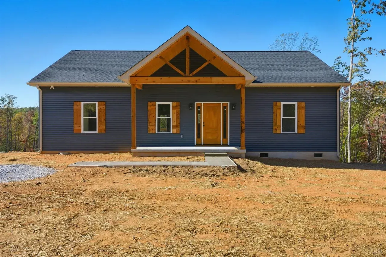 A single-story blue house with wooden trim, a covered porch, and a gable roof, set on a plot of unlandscaped dirt.