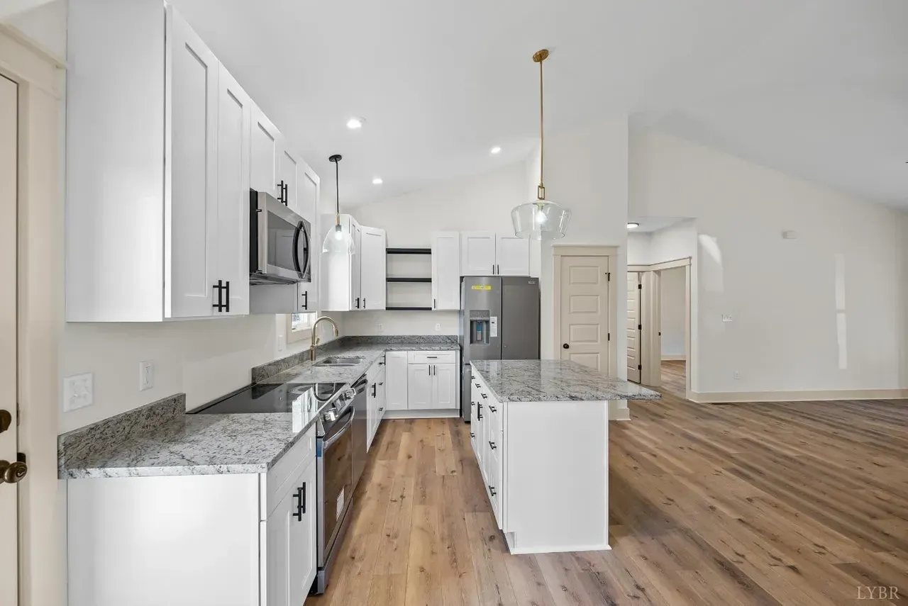 A bright, modern kitchen with white cabinets, granite countertops, stainless steel appliances, and wood-look flooring.