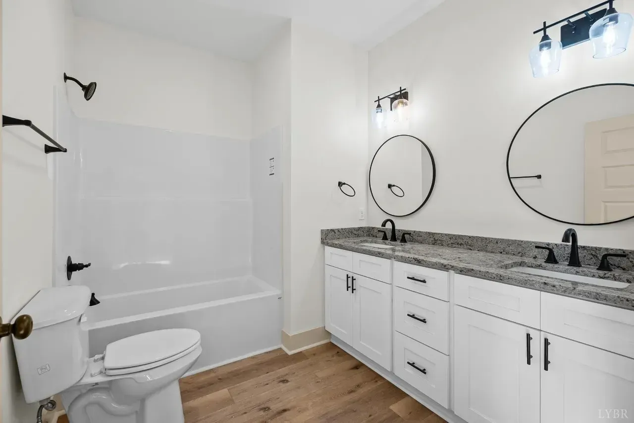A modern bathroom featuring a white double vanity, granite countertop, two round mirrors, and a white tub-shower combo.