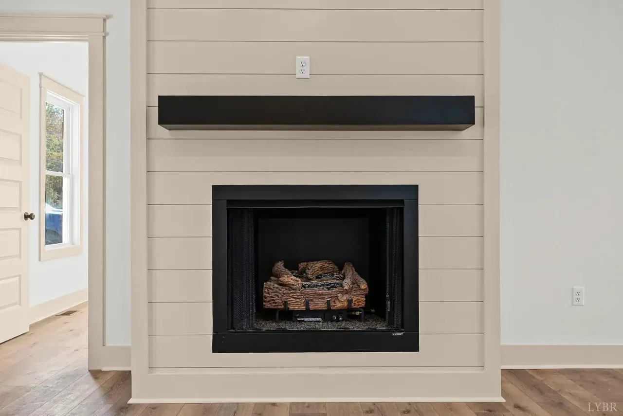 A beige shiplap fireplace with a black mantel and firebox, set against a white wall with light wood floors.