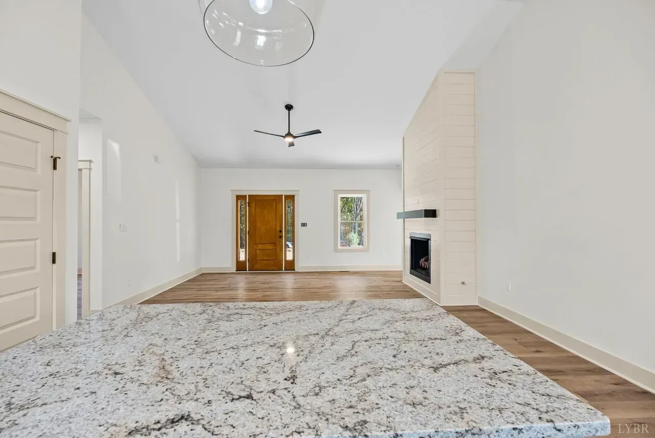 A modern, open-concept living space with white walls, wood floors, a fireplace, and a granite-topped kitchen island.