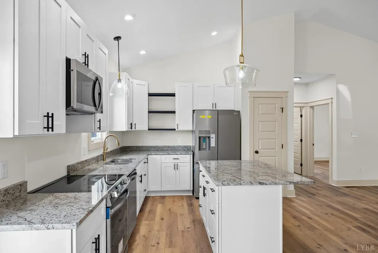 A modern kitchen with white cabinetry, granite countertops, stainless steel appliances, and wood flooring.