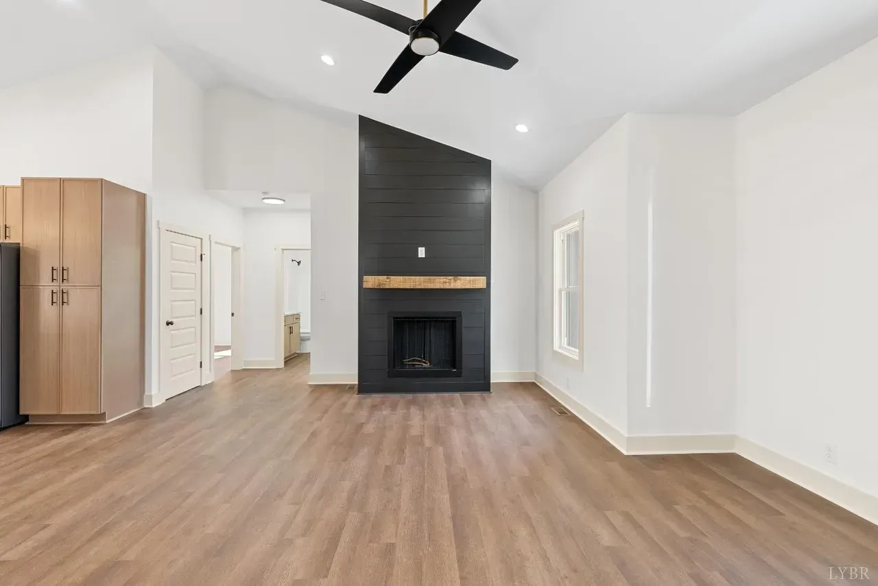 A bright living room with wood floors, white walls, and a tall fireplace feature wall with horizontal black planks.