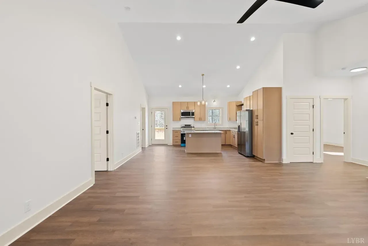 A bright, open-concept kitchen and living area with wood floors, light-toned cabinets, a kitchen island, and white walls.