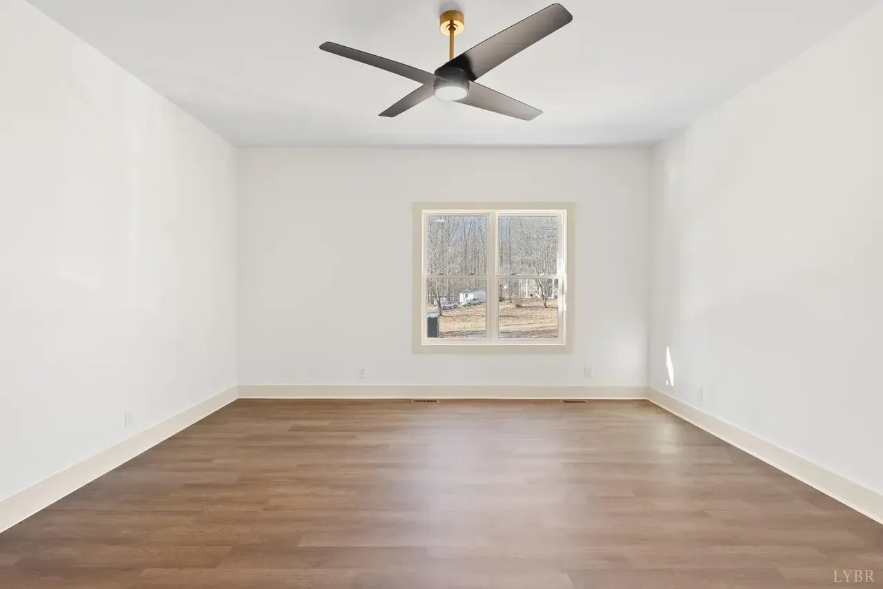An empty room with white walls, wood-look flooring, a centered window, and a ceiling fan.
