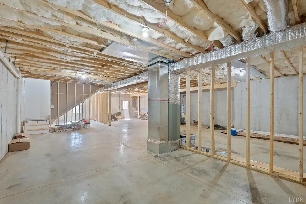 An unfinished basement with exposed wooden studs, concrete floors, and insulation visible on the ceiling joists.