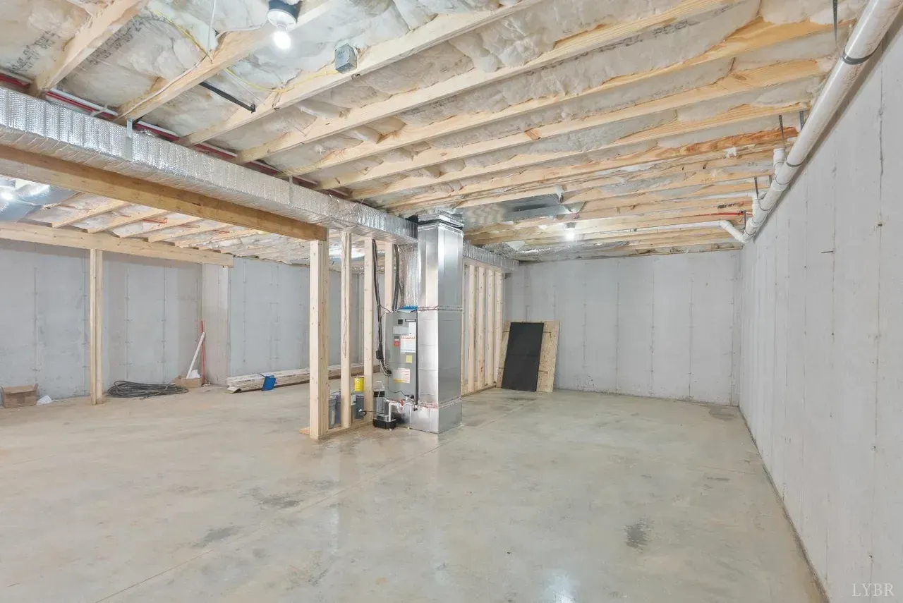 An unfinished basement with exposed wooden joists, concrete walls, a cement floor, and a central HVAC furnace unit.