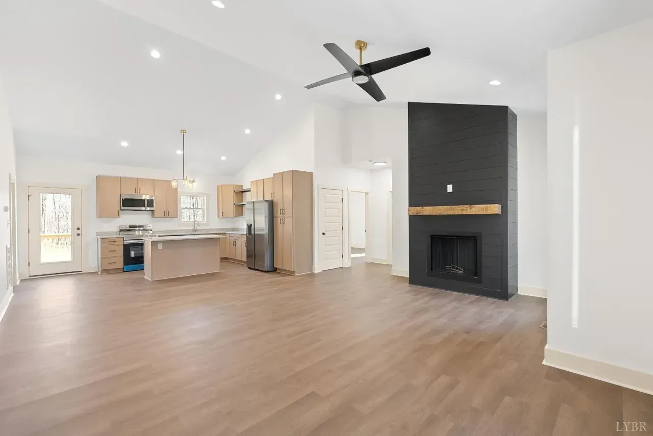 An open-concept living area with light wood flooring, a modern kitchen with island, and a black fireplace with a mantle.