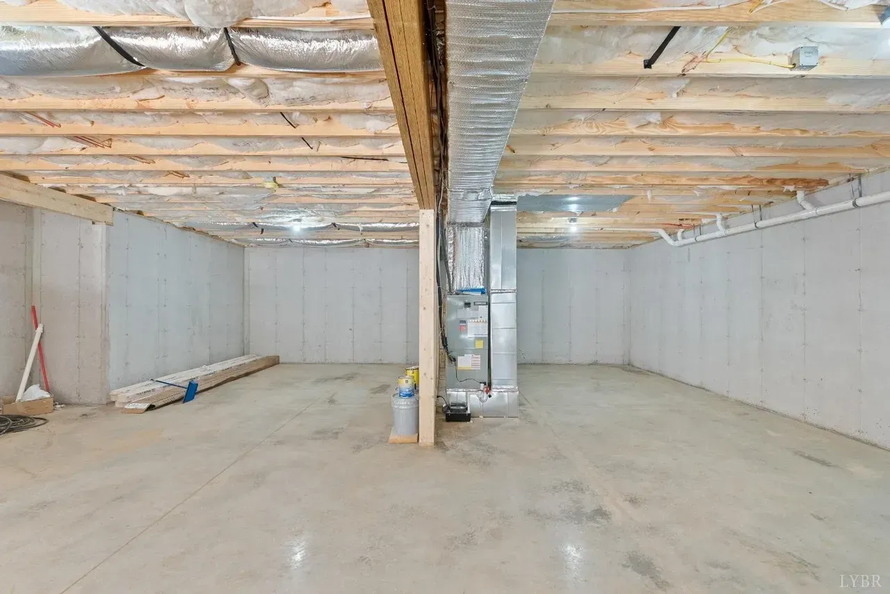 An unfinished basement with concrete walls and floors, exposed ceiling joists, and a central HVAC unit.